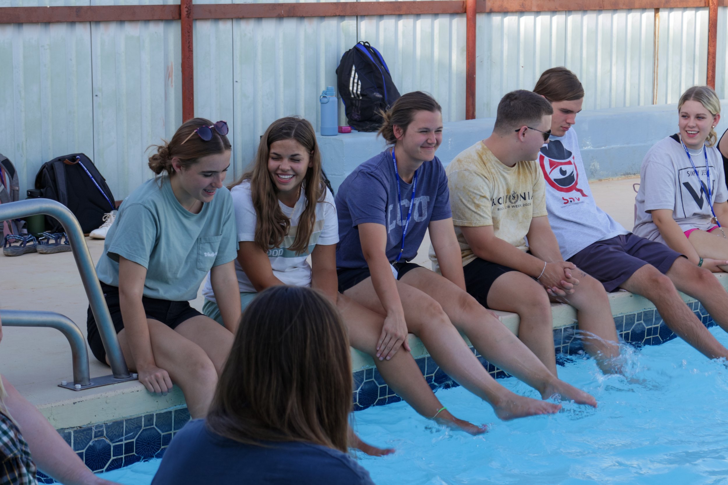 Students smiling and sitting around a swimming pool with their feet in the water