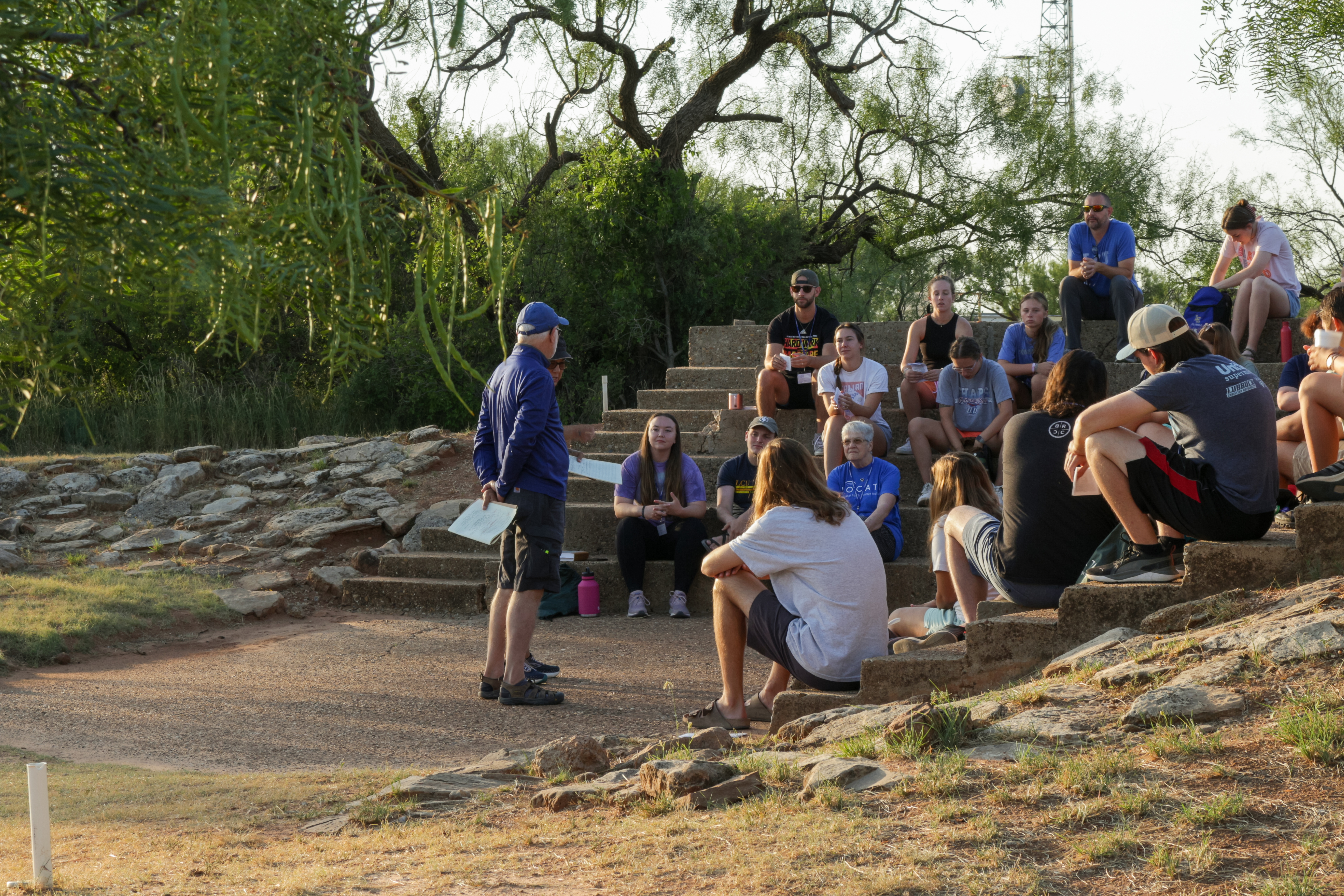 Students sitting around a min in a blue shirt giving a lecture