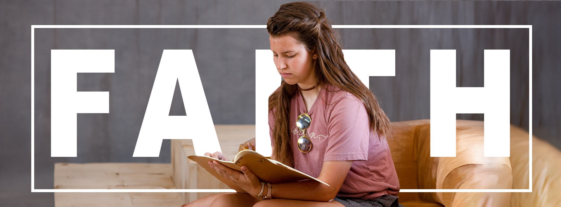 A girl writing in a journal with the word "FAITH" behind her and the words "Vocati July 28-Aug 2" written in the top left corner.