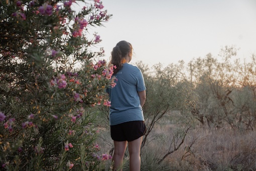 Flowers and trees with a student with their back facing the camera, looking out.