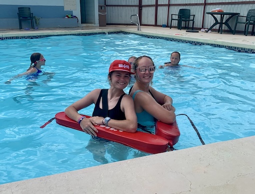 Campground swimming pool with lifeguards smiling and students swimming in the background